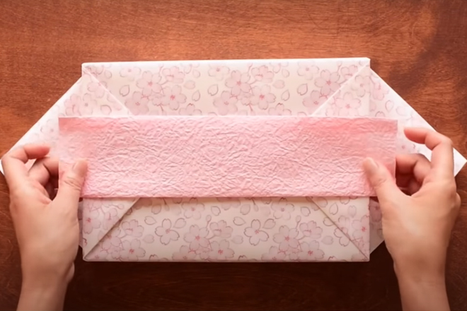Dùng băng dính hai mặt để chuẩn bị dán miếng giấy lên hộp quà.