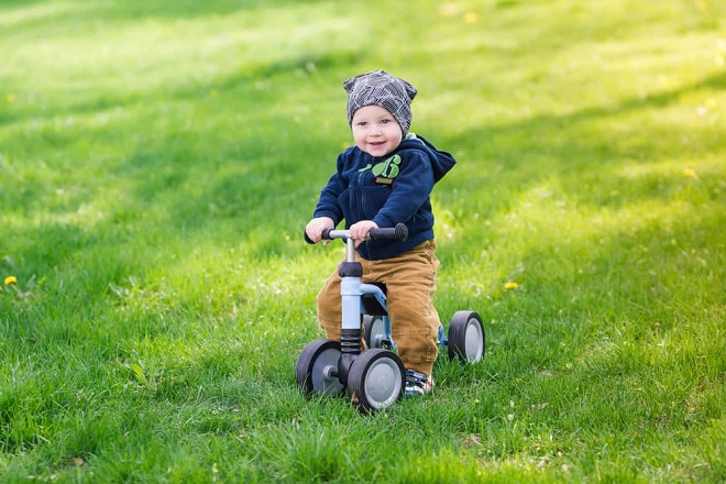 Trẻ chạy xe ba bánh trên bãi cỏ